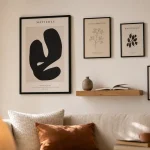 Décorer mur blanc avec cadres, étagère flottante et lumière naturelle.